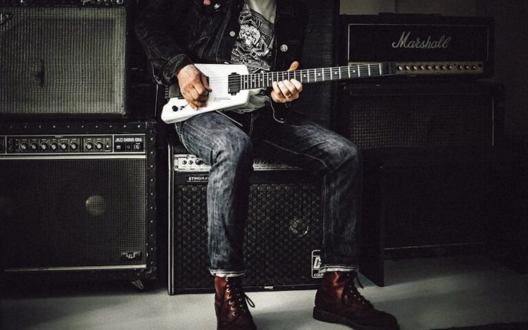 man sits on an amp holding a guitar