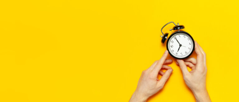 hands holding an old-fashioned clock on a yellow background