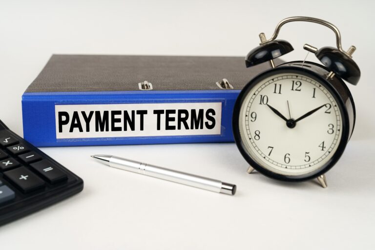 Blue binder labeled payment terms next to a clock and a pen